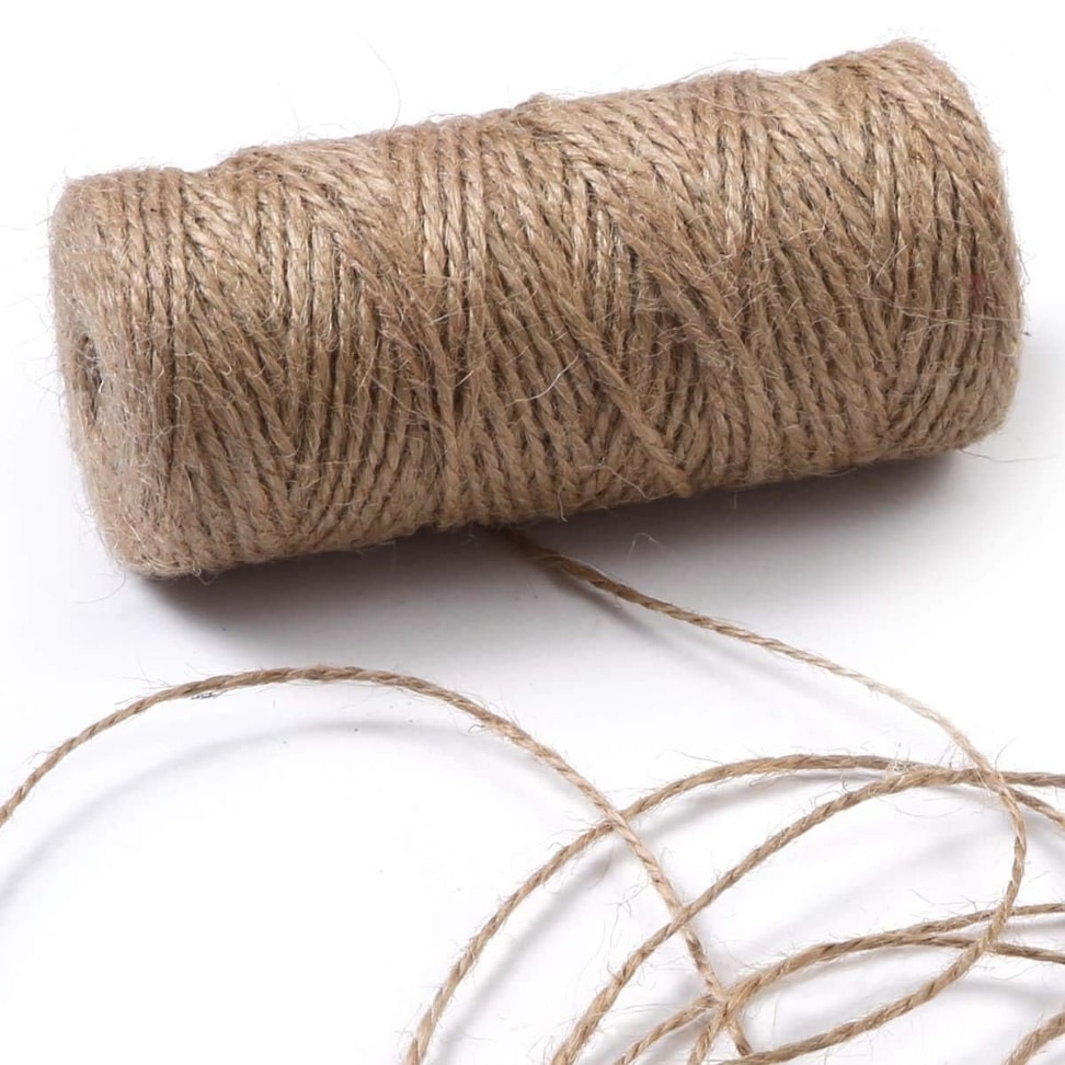 A spool of natural brown twine with several loose strands extending from it, perfect for your next DIY project or crafting a rustic garland, lies elegantly on a white surface.